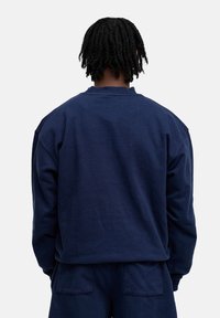 Marineblaues Sweatshirt mit langen Ärmeln, Rundhalsausschnitt, überschnittenen Schultern und strukturiertem Material. Keine sichtbaren Logos oder Akzente.