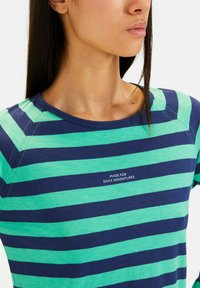 Gestreept t-shirt met marineblauwe en teal horizontale strepen, ronde halslijn en tekst "MADE FOR DAILY ADVENTURES" in het wit. Zachte stof.