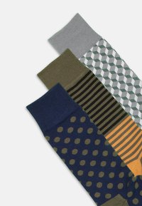 Drei Paar Socken: marineblau mit grünen Punkten, olivgrün mit Streifen und grau mit geometrischen Mustern. Aus gestricktem Material, unterschiedlich lange Längen.