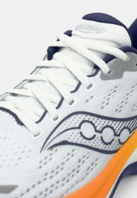 Valge sportlik king, millel on võrgu pealis, sinised aktsendid, hallid disainimustrid ja oranž tall. Omab valgeid paelu ja tekstureeritud pinda.