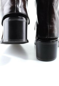 Paire de bottes en cuir marron foncé avec talons blocs vues de dos sur une surface blanche.