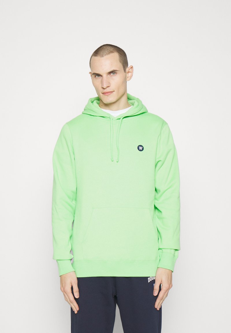 Grønn bomull hettegenser med kengurulomme, justerbare snører og en liten marineblå logo på brystet. Lange ermer og ribbestrikkede mansjetter.