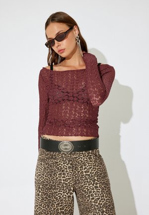 Bordeaux kanten lange mouwen top, gelaagd over een zwarte tank, gecombineerd met een panterprint brede broek en een zwarte riem met een zilveren gesp.