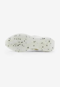 Suela de zapato con un material blanco translúcido, que presenta un patrón negro moteado y un diseño de agarre con patrones para tracción.