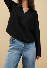 Blusa nera a maniche lunghe con tessuto testurizzato e scollatura a V, abbinata a jeans blu a vita alta. Design semplice, senza motivi o accenti.