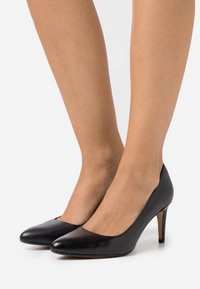 Escarpins en cuir noir avec bout pointu, design élégant et talon aiguille. Texture lisse avec une silhouette classique et des détails minimalistes.