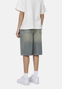 Shorts in denim di colore azzurro chiaro con una finitura sbiadita, caratterizzati da una vestibilità regolare, un taglio lungo fino al ginocchio, tasche posteriori e orlo pulito. Indossati con sneakers bianche.