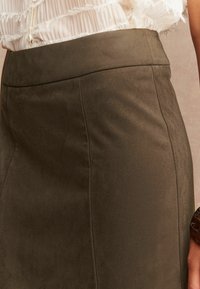 Hnědá semišová sukně s hladkým povrchem, vysokým pasem a přiléhavým střihem, s čistými liniemi a minimalistickými švy.