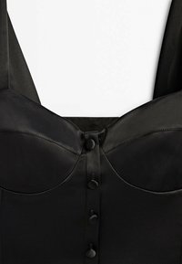 Black satin top with structured cups, thick straps, and five vertical buttons down the center; smooth texture with a sleek finish.