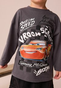 Rifle šedá mikina s dlouhým rukávem s grafickým motivem blesku McQueen v oranžové barvě, tučným černobílým textem a kostkovaným vzorem na spodní části.