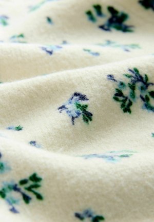 Kremo spalvos audinys su minkšta, tekstūruota paviršiumi, kuriame išsibarsčiusios subtilios gėlių motyvų mėlynos ir žalos atspalvių detalės.