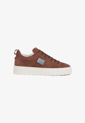 Brown suede low-top sneaker with thick white platform sole, brown laces, and a rectangular silver logo patch on the side.