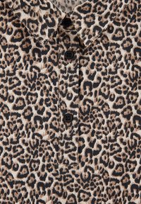 Leopardo rašto polo marškiniai su mygtukų užsegimu, juodais mygtukais ir tekstūruotu audiniu smėlio ir rudos spalvos atspalviais.