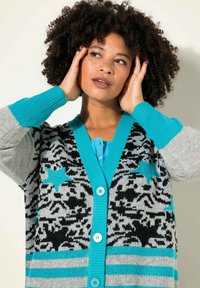 Cardigan a maglia con una base grigia e motivi neri e turchesi, colletto a V e bottoni blu. Le maniche sono turchesi con strisce grigie.