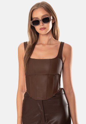 Brauner Kunstleder-Corsagen-Top mit quadratischem Ausschnitt, breiten Trägern und strukturierten Nähten. Getragen mit dunklen, hoch sitzenden Lederhosen und Sonnenbrille.