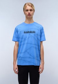 T-shirt in cotone blu con un motivo a onde testurizzato e una stampa del logo nera al centro. Vestibilità rilassata con maniche corte.
