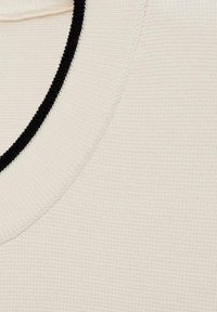 Tissu beige clair avec un motif texturé côtelé ; présente un col arrondi bordé de noir. Le matériau semble doux et tricoté.