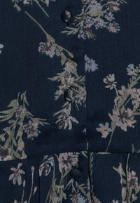 Tissu marine avec un motif floral dans des verts et des roses atténués, comportant des boutons noirs et une finition texturée.