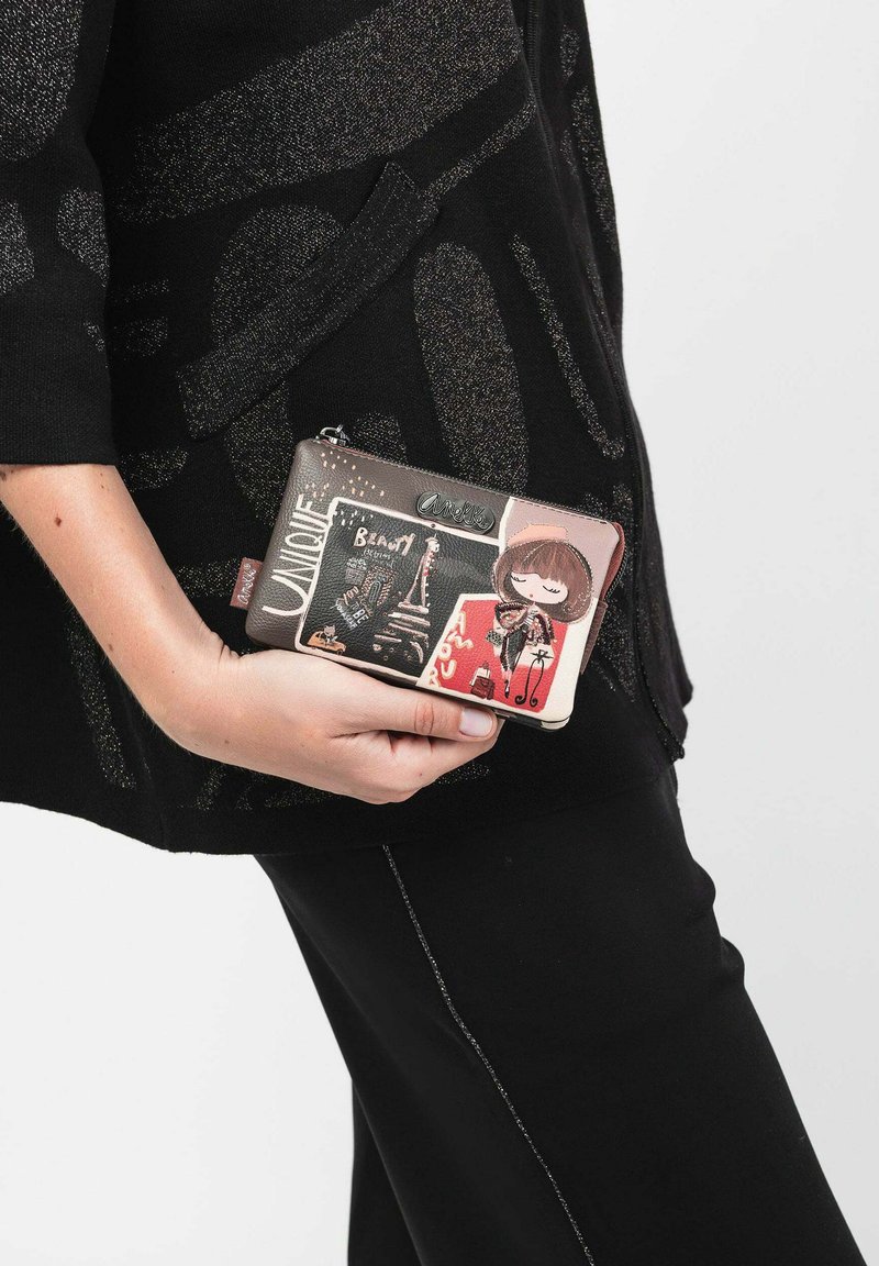Portafoglio multicolore realizzato in materiale sintetico con illustrazioni, dotato di chiusura con zip e accenti grafici, tenuto in mano su uno sfondo scuro.