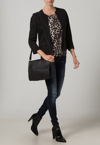 Schwarzer Blazer über einem Leopardenmuster-Oberteil, kombiniert mit dunklen Skinny-Jeans und schwarzen Stiefeletten mit Absatz. Eine schwarze Ledertasche rundet den Look ab.