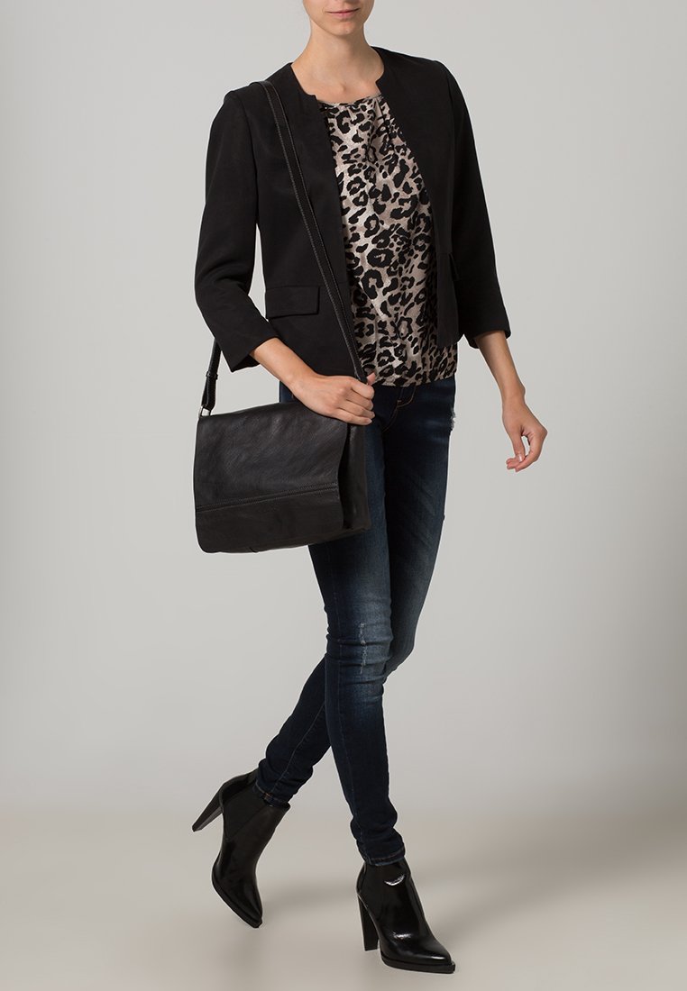Schwarzer Blazer über einem Leopardenmuster-Oberteil, kombiniert mit dunklen Skinny-Jeans und schwarzen Stiefeletten mit Absatz. Eine schwarze Ledertasche rundet den Look ab.