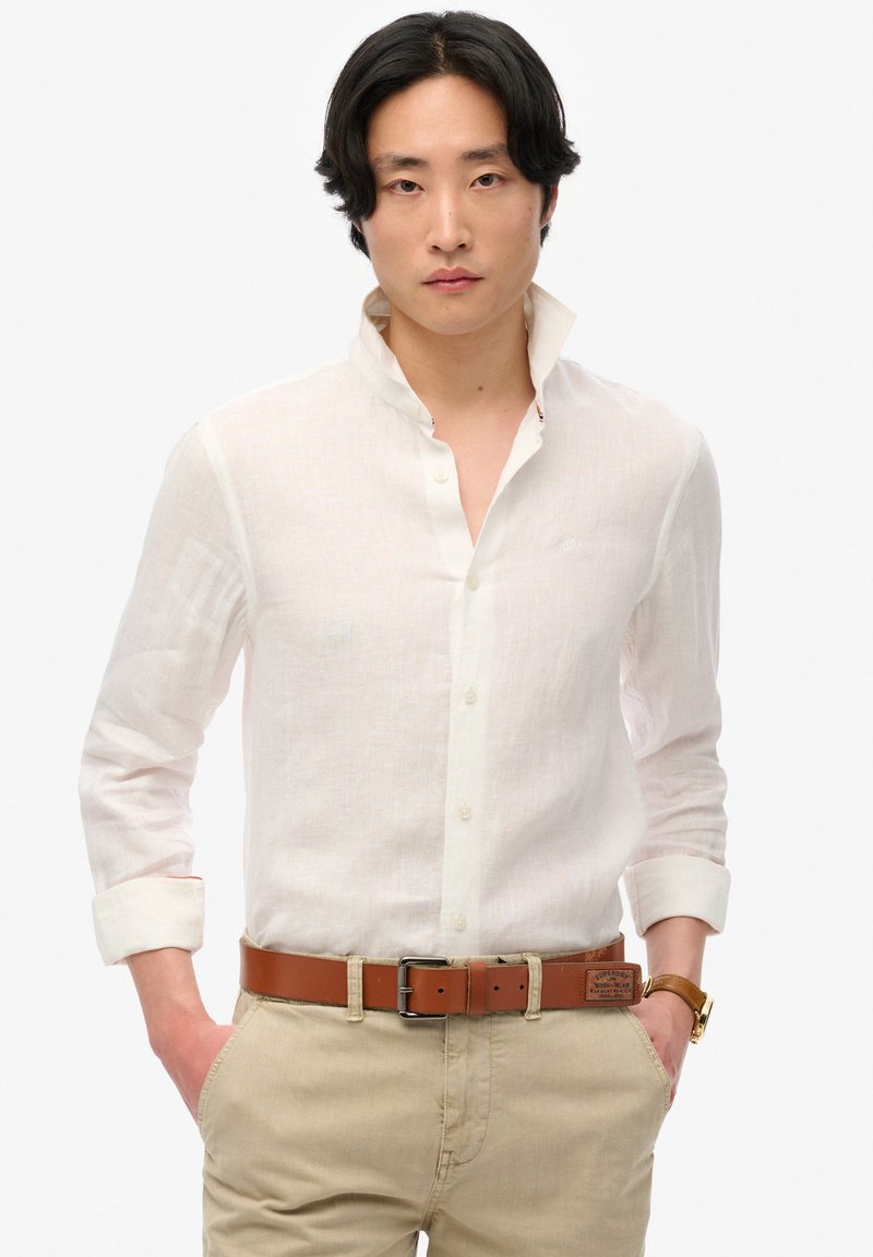 Witte linnen overhemd met een button-down kraag, opgerolde mouwen, gecombineerd met tan chino's en een bruine leren riem. Subtiele textuur en ontwerpdetails.