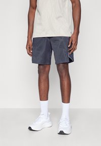 Shorts con estampado de marina y diseños geométricos, combinados con una camiseta de patrón gris claro y zapatillas y calcetines blancos. Tejido suave, corte casual.