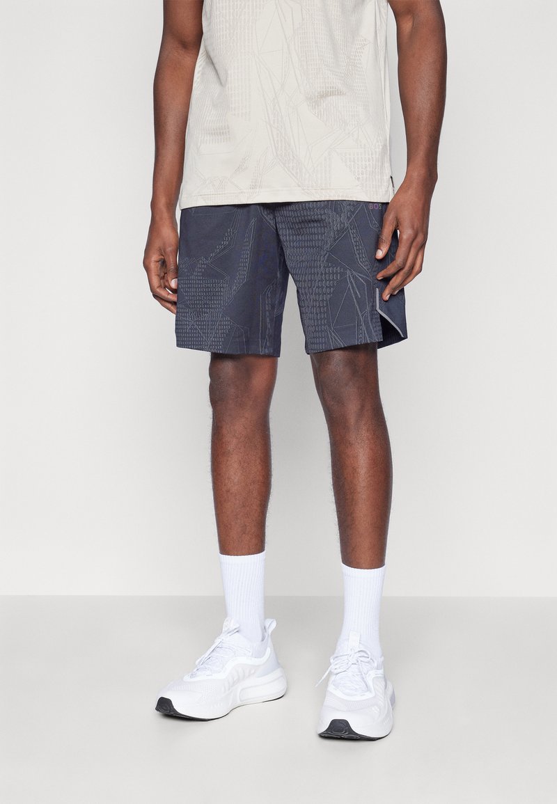 Shorts con estampado de marina y diseños geométricos, combinados con una camiseta de patrón gris claro y zapatillas y calcetines blancos. Tejido suave, corte casual.
