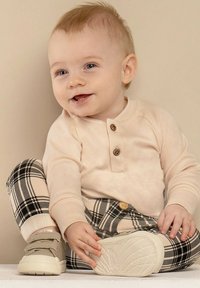 Bladoróżowa koszula z długim rękawem i zapięciem na trzy guziki; spodnie w czarno-beżową kratę; jasne buty na rzepy.