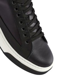 Sneaker nera con tomaia in pelle liscia, chiusura con lacci neri e suola intermedia bianca con suola esterna in gomma nera texturizzata.