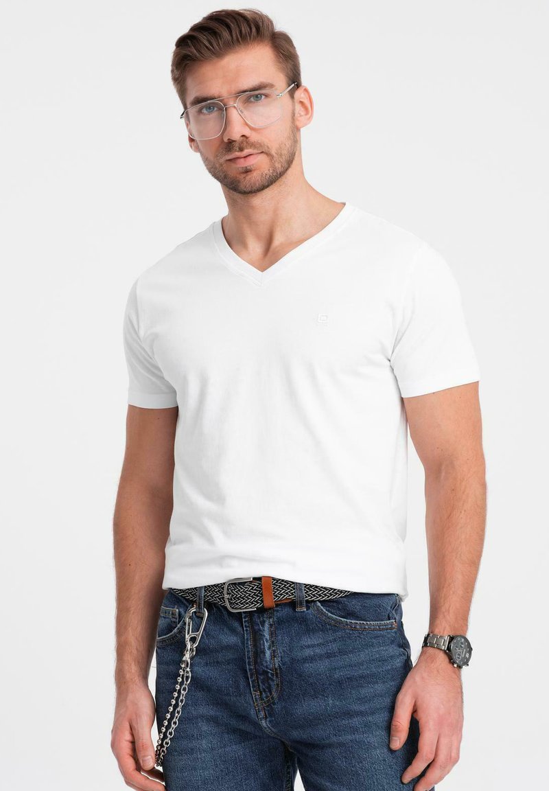 Hvid bomulds V-hals t-shirt med korte ærmer, parret med blå denim jeans. Har et mønstret sort bælte og et sølvur på håndleddet.