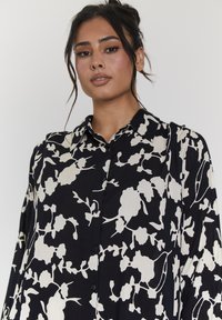 Camicia a maniche lunghe con bottoni in un motivo floreale bianco e nero, realizzata in tessuto leggero con colletto e vestibilità rilassata.