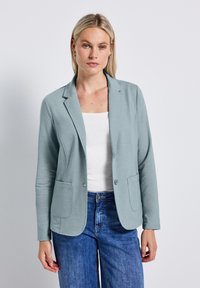 Světle modrý blazer z měkké tkaniny, s výstřihem do "V", dvěma předními kapsami a uvolněným střihem. V kombinaci s bílým topem a modrými džíny.