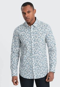 Lange mouw overhemd van lichte stof met een witte basis, voorzien van een blauw loofpatroon, knoopsluiting bij de kraag en manchet mouwen.