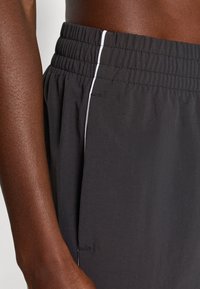 Melnu sporta šortus ar elastīgu jostu, kas papildināti ar baltu akcenta svītru gar sānu un gludu, vieglu auduma tekstūru.