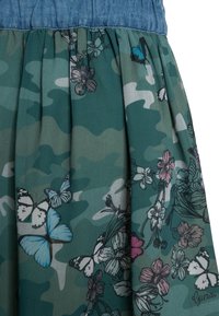 Spódnica w kwiatowy wzór z zielonym kamuflażem, wykonana z prześwitującego materiału. Posiada plisowania i jeansowy pas w talii.