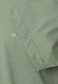 Olivgrön kortärmad skjorta med slät textur, med en diskret logobrodering nära ärmen och kontrasterande sömnaddetaljer.