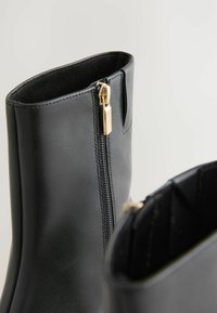 Stivaletti neri in pelle con finitura liscia, caratterizzati da un dettaglio in zip dorata lungo il lato e una parte superiore arrotondata.