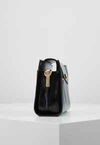 Černá a šedá kožená kabelka s texturovaným povrchem, horním uchem a zlatými kovovými detaily, se čtvercovým tvarem a hladkými stranami.