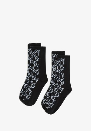Czarne skarpetki o prążkowanej teksturze, z powtarzającym się białym geometrycznym wzorem. Krótkie, sięgające kostki, z wzmocnionym palcem i piętą.