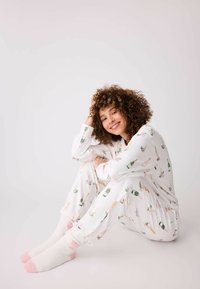Vit pyjamas-set med blommönster och champagneflaskor, mjukt tyg, kombinerat med vita fluffiga strumpor med rosa detaljer.