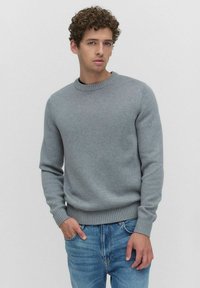 Grijze gebreide trui met een ronde hals en geribbelde manchetten, gecombineerd met lichtblauwe jeans. Klassiek ontwerp en soepele textuur.