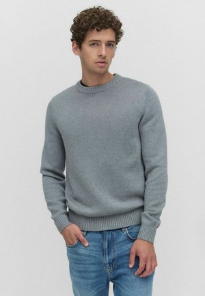 Grijze gebreide trui met een ronde hals en geribbelde manchetten, gecombineerd met lichtblauwe jeans. Klassiek ontwerp en soepele textuur.