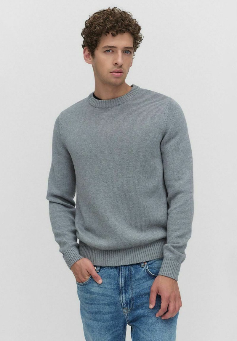 Grijze gebreide trui met een ronde hals en geribbelde manchetten, gecombineerd met lichtblauwe jeans. Klassiek ontwerp en soepele textuur.