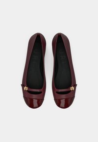 Μπαλαρίνες από πατέντα δέρμα σε μπορντό χρώμα με στρογγυλεμένη μύτη, διακοσμημένες με χρυσά μεταλλικά στοιχεία και λεπτομέρειες με κοψίματα κοντά στο πάνω μέρος του ποδιού. Μαλακή μαύρη εσωτερική επένδυση.