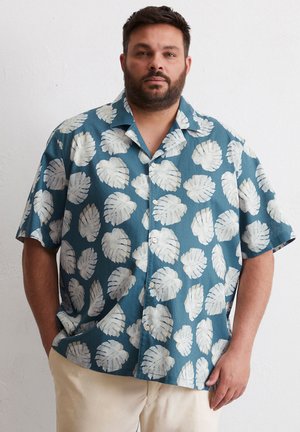 Chemise à manches courtes en tissu teal avec un motif de feuilles blanches. Le tissu a une texture lisse et une coupe décontractée.