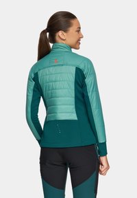 Turbukiet i ciemnozielona kurtka z pikowanym górnym sectionem, gładkim dolnym materiałem, wysokim kołnierzem i małymi dekoracyjnymi akcentami z tyłu.