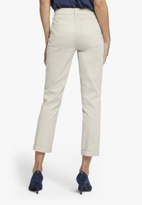 Béžové bavlněné kalhoty s ohrnutými nohavicemi, dvěma zadními kapsami a středním pasem. Nosit s námořnickým modrým vysokým podpatky.