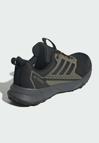 Schwarzer Sportschuh mit Mesh-Obermaterial, grauer Gummisohle und roten Akzenten. Verfügt über drei schwarze Streifen und eine Zuglasche an der Ferse.