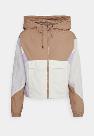 Veste coupe-vent courte avec un design en blocs de couleur beige, blanc et lilas, capuche ajustable et fermeture éclair à l'avant avec deux poches.